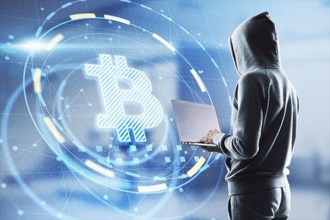 hacker in hoodie using laptop computer with glowing bitcoin interface in blurry office interior hacking, theft and cryptocurrency concept double exposure