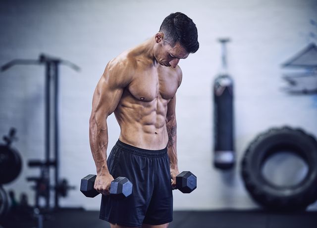 muscular male bodybuilder in industrial gym holding dumbbells