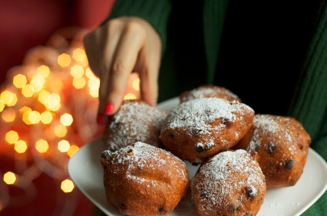 traditional dutch new years eve pastry   oliebollen, woman picking one donut, bokeh lights background
