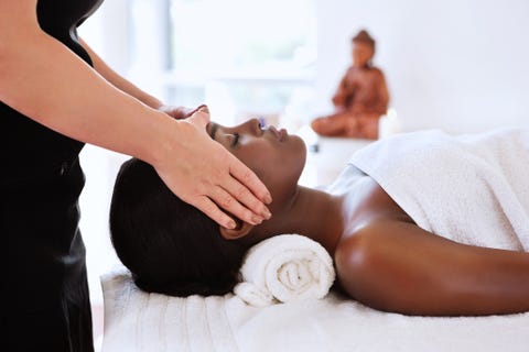 Woman receives a head massage from a masseuse a Buddha statue sits in the background horizontal shot