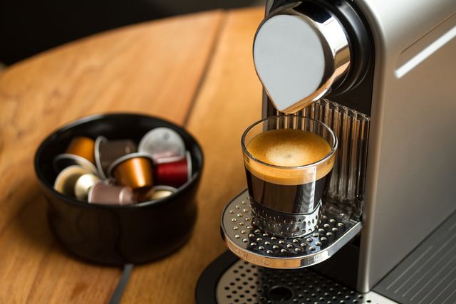 copenhagen, denmark   july 8, 2014 freshly brewed espresso in glass standing on silver nespresso coffe machine blurred background with nespresso capsules in black bowl