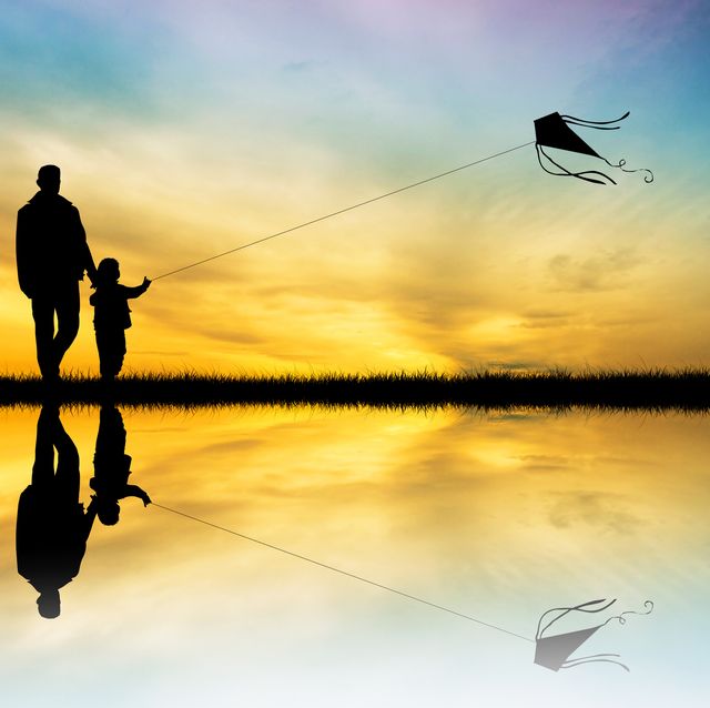 black silhouettes of father and son with kite at sunset