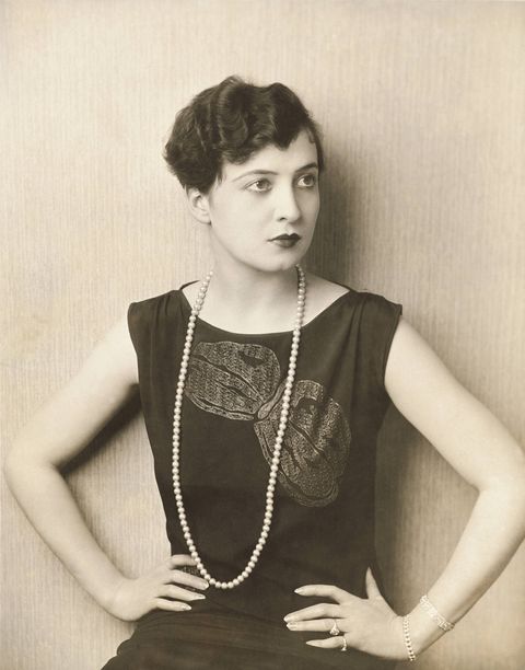 half length portrait of american actress, mary duncan, seated with both hands on hips head turned to side wearing a sleeveless black dress with large embroidered bow detail on chest, two diamond bracelets on left wrist, two rings on left hand, and a long string of pearls hair is in a pixie cut with finger waves photo by florence vandammcondé nast via getty images