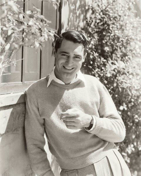 cary grant, outside, smiling, wearing a crewneck sweater over a white shirt, pleat front pants, holding a cigarette photo by george hoyningen huenecondé nast via getty images