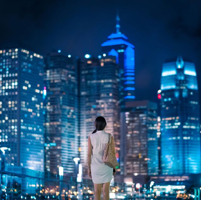 rear view of asian female overlooking and enjoying the stunning view of modern city night scene, with massive illuminated corporate highrise buildings in the background