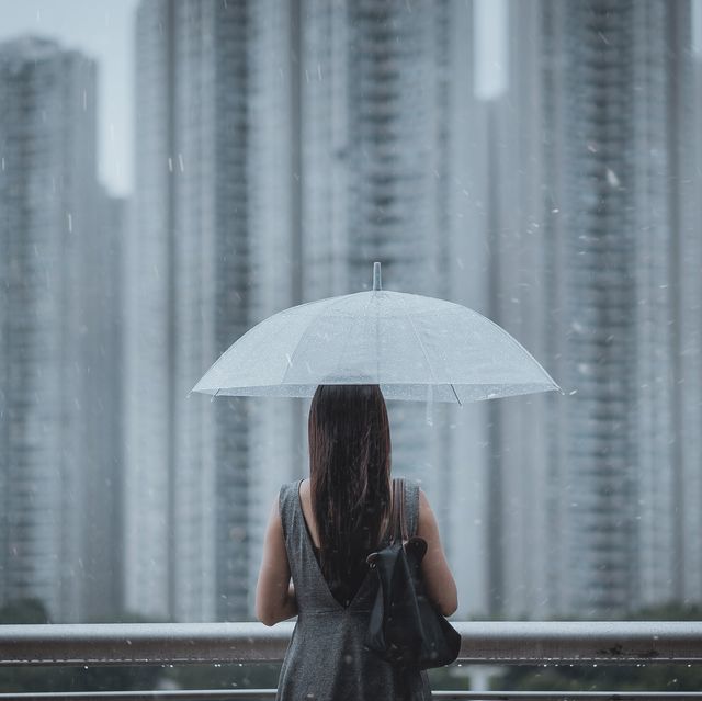rear view of young businesswomen with umbrella overlooking the city on a rainy and gloomy day, with blurry highrise residential blocks in the background