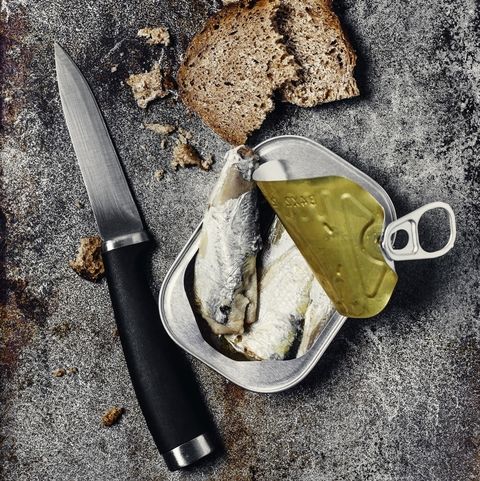 can of sardines with a whole grain slice of bread and a knife on metal background