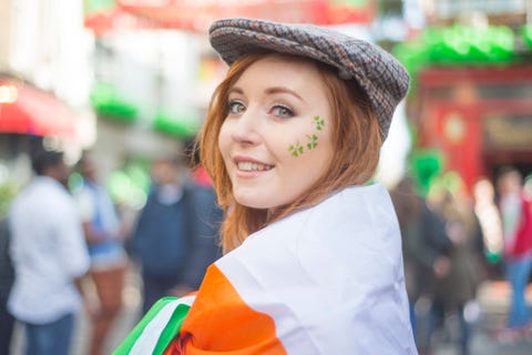 smiling pretty red haired irish girl with tweed hat, wrapped in the irish flag and shamrocks painted on her face, temple bar, dublin, ireland