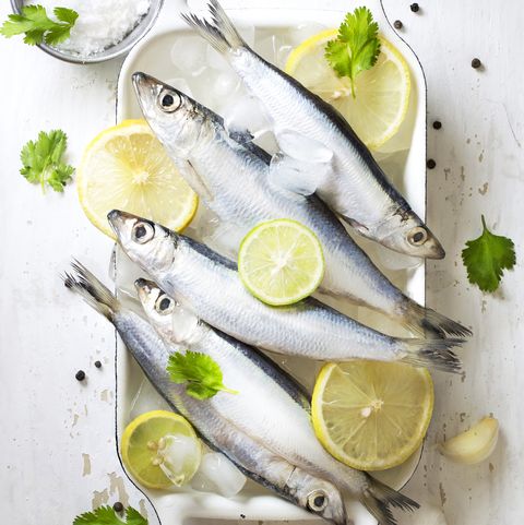 Chilled fresh uncooked sardines with herbs and lemon slice on white background.