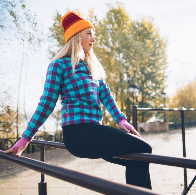 young beautiful woman relaxing during street workout sitting on parallel bars at calisthenics park, looking off the camera