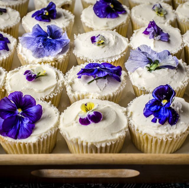 closeup of a tray of frosted vanilla cupcakes decorated with edible flowers such as pansies and violets