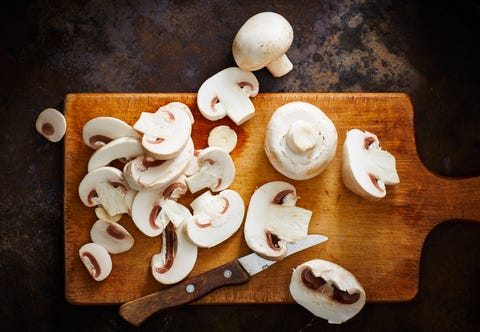 Whole and chopped champignons and kitchen knife on wooden board