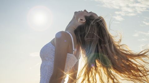 een vrouw gooit haar haren naar achter in de zon