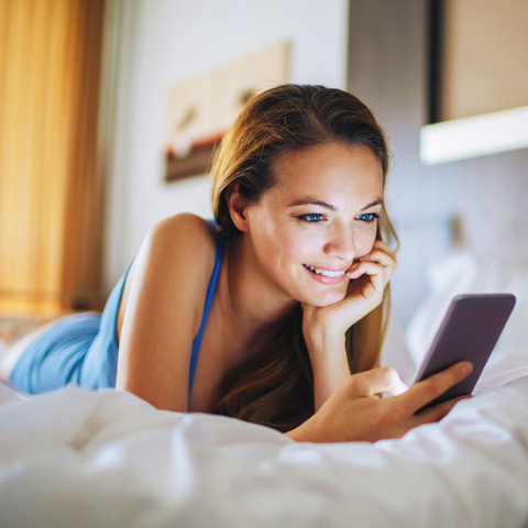 Photo of a young woman laying in bed using smartphone