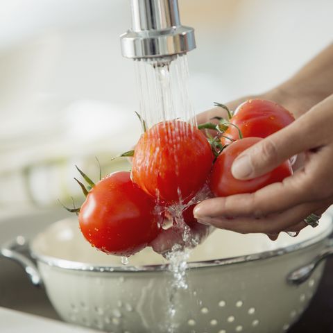 Mid-adult woman rinsing tomatoes in sink with colander.