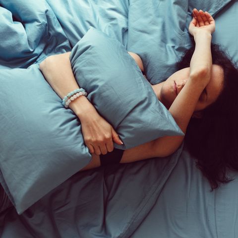 A sick young woman in bed covering her body with a pillow and her hand with her face.