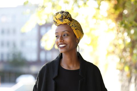 beautiful, young, happy muslim woman photographed in an bright outdoor urban setting wearing a yellow, decorated wrap around her head