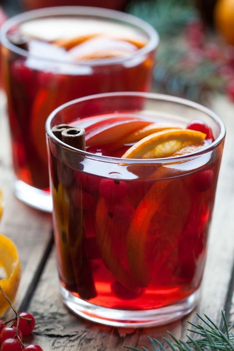 Homemade mulled wine or sangria with orange slices, cranberries, cinnamon on wooden table. Christmas tree decorations