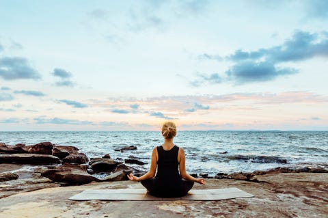 Young woman performs yoga moves on bluff above sea