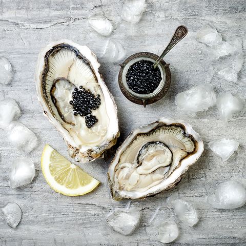 opened oysters with black sturgeon caviar and lemon on ice on grey concrete background top view, flat lay, copy space