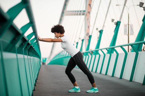an athletic woman warming up before she starts to run on city bridge
