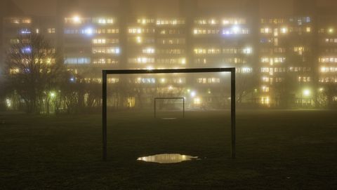 Sweden, Skane, Malmo, Rosengard, Illuminated residential buildings with soccer field in foreground in fog
