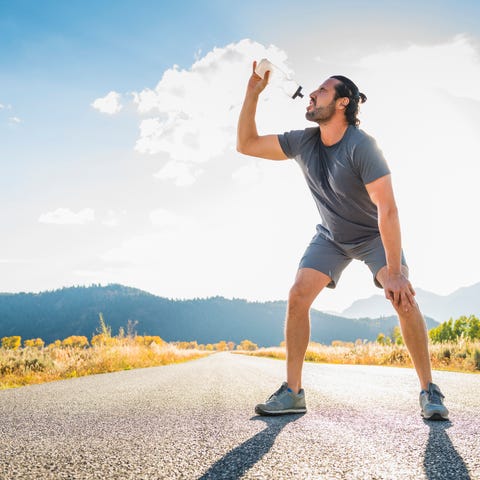 Hispanic runner drinking water in middle of road dude chugging h20 on an empty stretch of street by the mountains