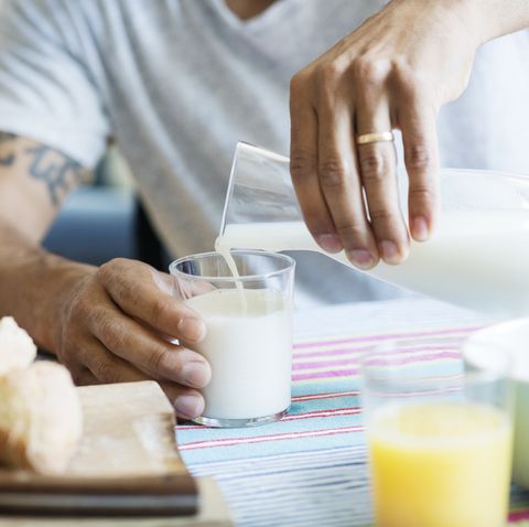 midsection of man pouring milk in drinking glass at tablemidsection of man pouring milk in drinking glass at table