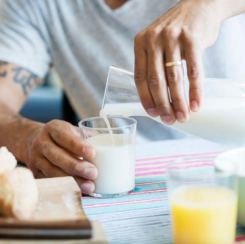 midsection of man pouring milk in drinking glass at tablemidsection of man pouring milk in drinking glass at table