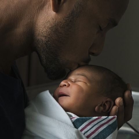 Black father kissing forehead of newborn son