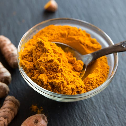 Glass bowl of curcuma powder and fresh organic curcuma on slate