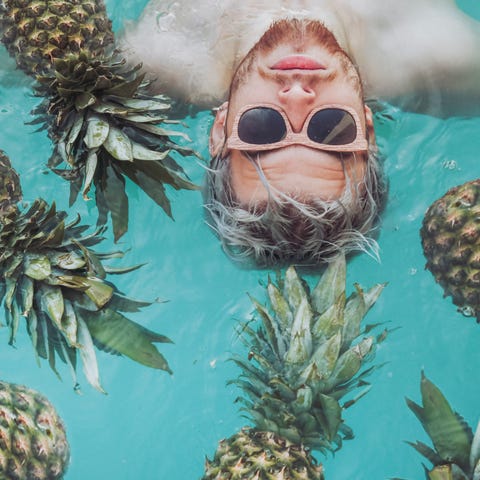 Young man in swiming pool surrounded by pineapples man swimming with pineapples
