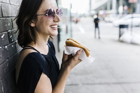Smiling woman with Hot Dog leaning against wall
