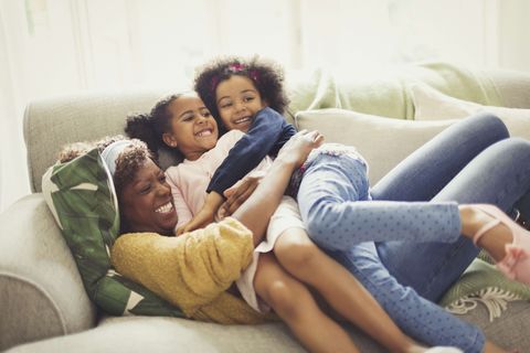 Playful mother and daughters cuddling on sofa