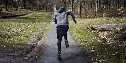 Full length rear view of determined male athlete jogging on narrow street in forest