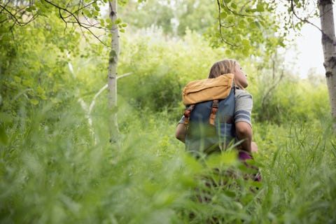 curious teenage girl with backpack hiking in tall grass in woods