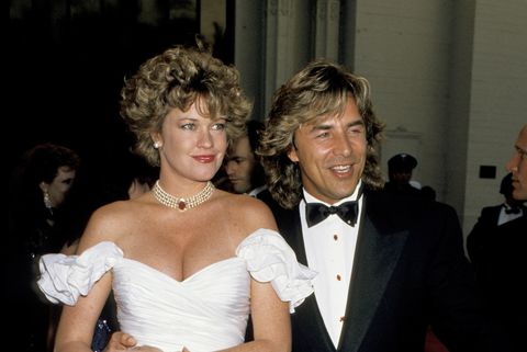 Melanie Griffith con vestido blanco y collar de perlas posa en la alfombra roja junto a su marido de entonces Don Johnson alrededor de los 80