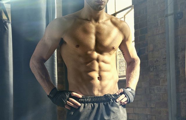 midsection of hispanic man standing near punching bags in gymnasium