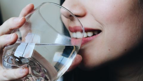Close-Up Midsection Of Young Woman Drinking Water At Home
