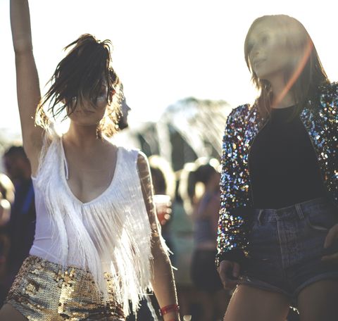 young woman at a summer music festival wearing golden sequinned hot pants, dancing among the crowd