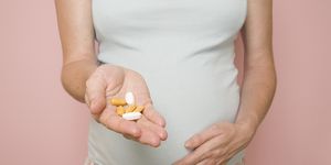 Torso of pregnant woman with handful of vitamins