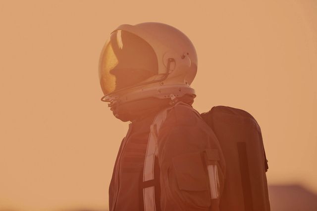 portrait of astronaut in space suit and helmet on mars looking over towards left of camera, profile, with dust storm behind them, red orange planet