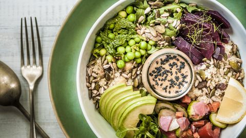 a healthy veganvegetarian lunch bowl of salads, grains, seeds, vegetables, avocado slices and a rich peanut miso sauce