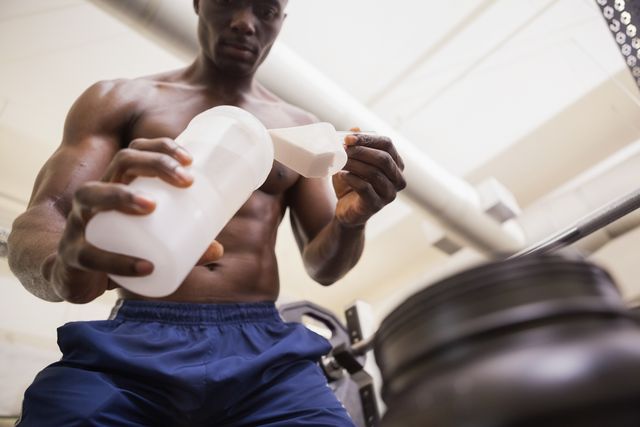 shirtless body builder scooping up protein powder in gym