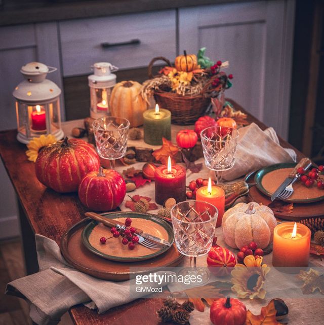 decorated table setting for thanksgiving dinner with candles, pumpkins, leafs and nuts