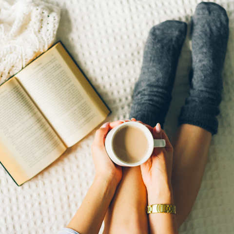 woman laying in bed and read book with cup if coffee.