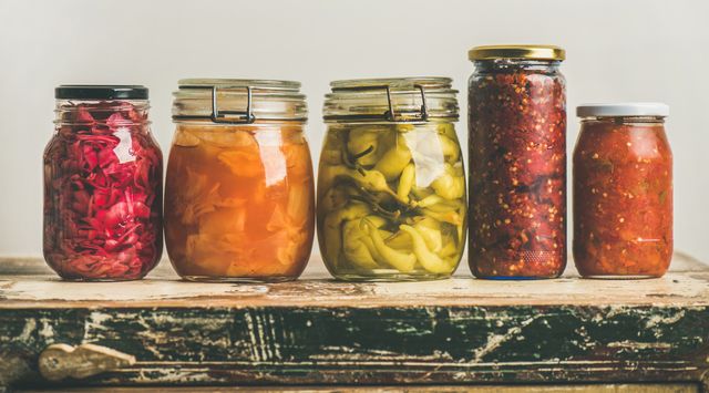 autumn seasonal pickled or fermented vegetables in jars placed in row over vintage kitchen drawer, white wall background, copy space fall home food preserving or canning