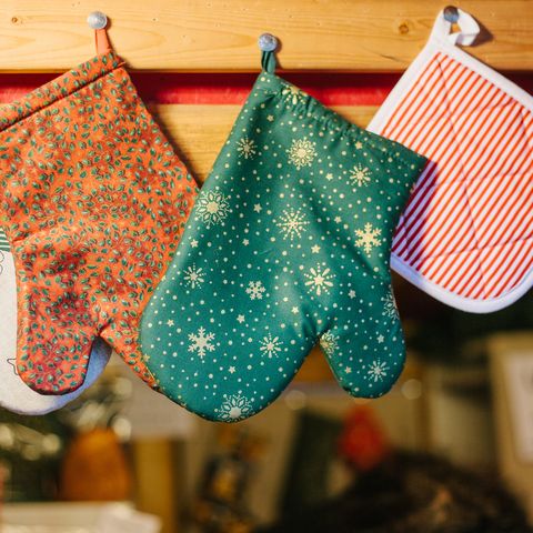 Christmas mittens potholders hang in kitchen against the background of blurry kitchen appliances.