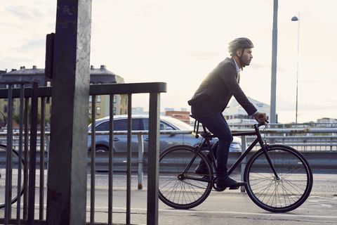 Side view of businessman cycling on street against sky