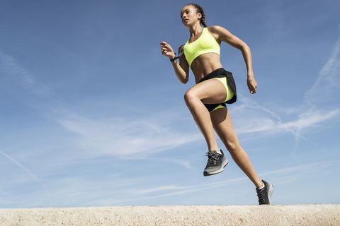 Low angle view of young female runner running along sea wall against blue sky